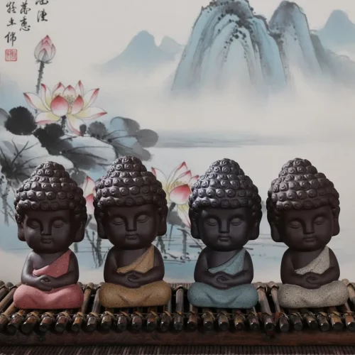 Set of four small Buddha statues in meditation pose displayed against traditional Chinese ink wash painting featuring lotus flowers and misty mountains