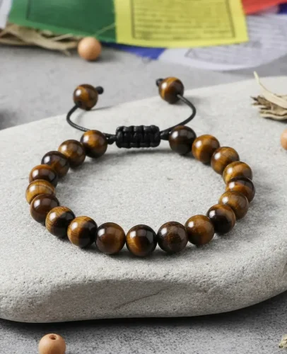 Natural tiger eye beaded bracelet with adjustable black cord on gray stone with colorful prayer flags