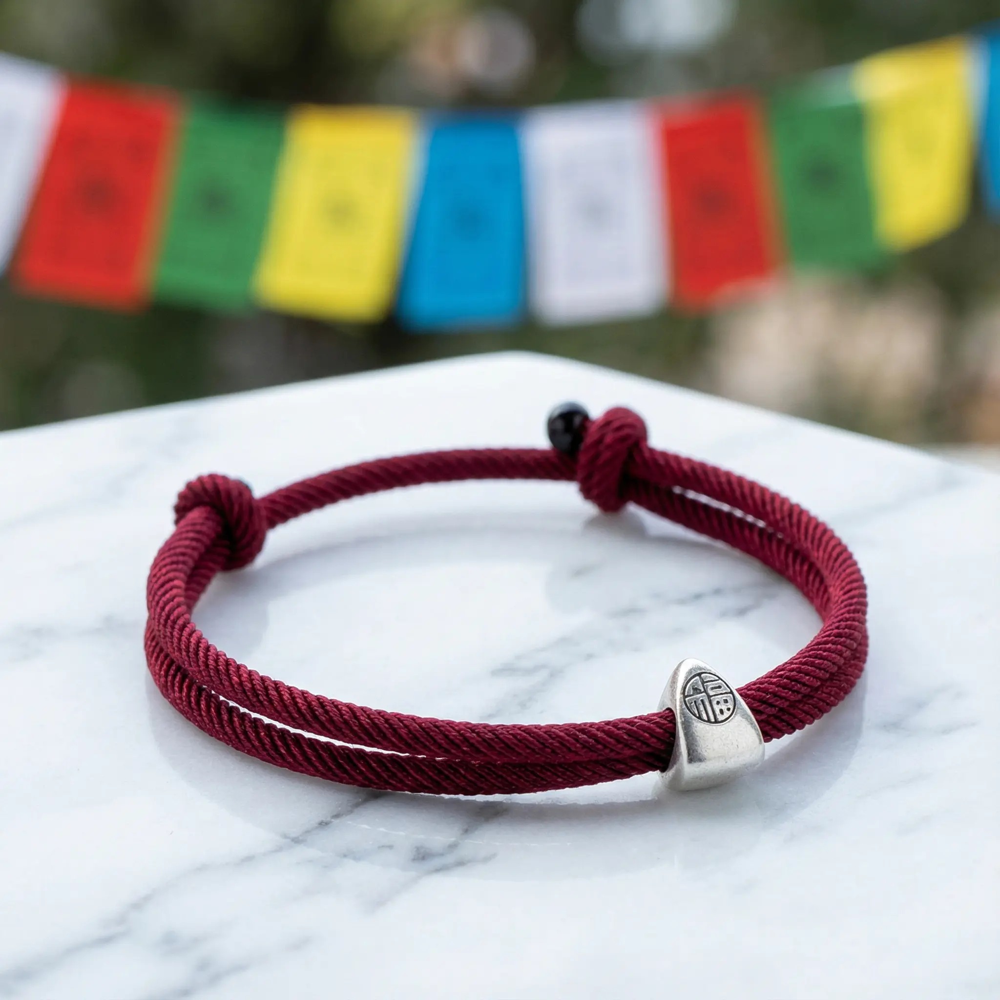 Tibetan Fu Symbol Red Cord Bracelet on Marble with Prayer Flags Tibetan fu symbol red cord bracelet on marble with prayer flags