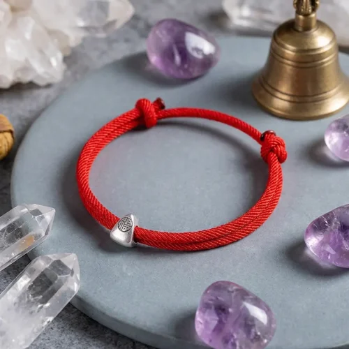 Red string Fu lucky bracelet surrounded by amethyst crystals, clear quartz and Tibetan bell on gray stone surface