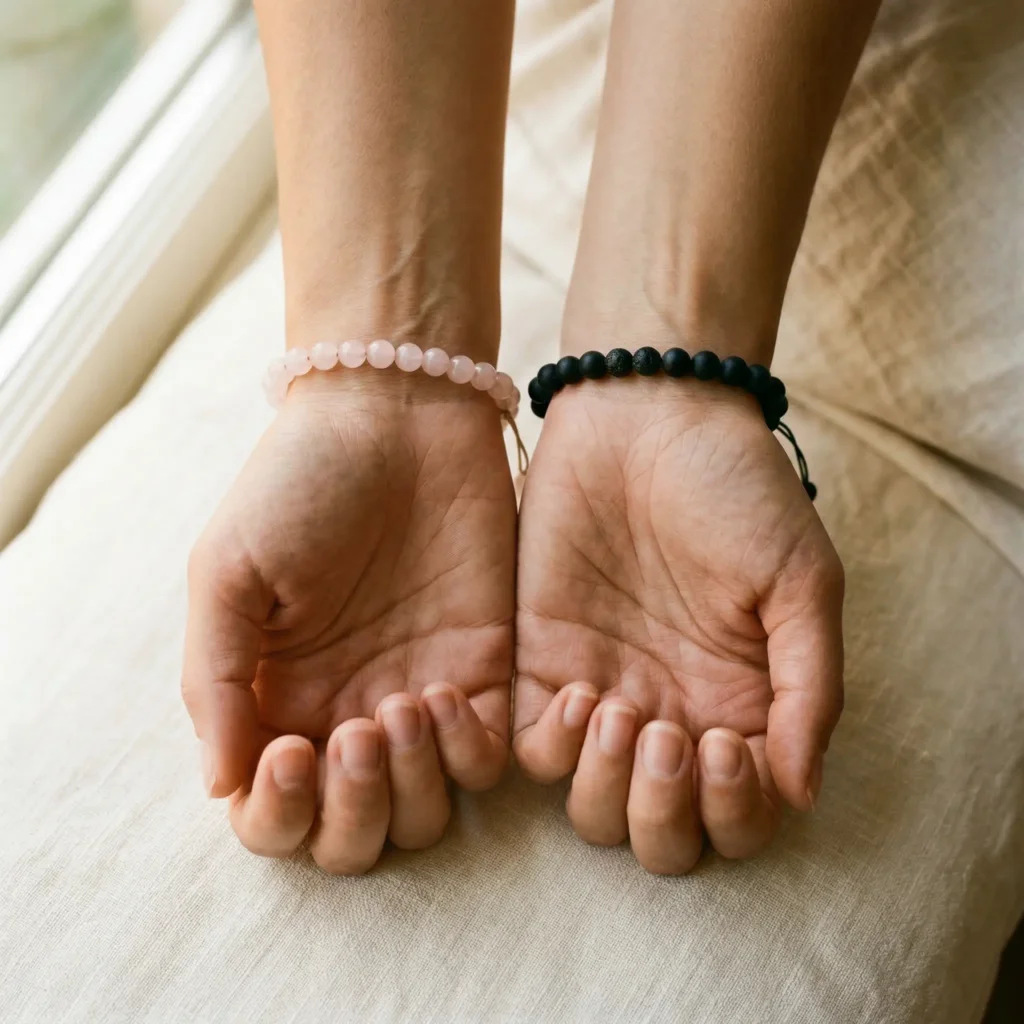 A woman's two wrists side by side, left wrist wearing a rose quartz bracelet for receiving energy, right wrist wearing a black tourmaline bracelet for protection