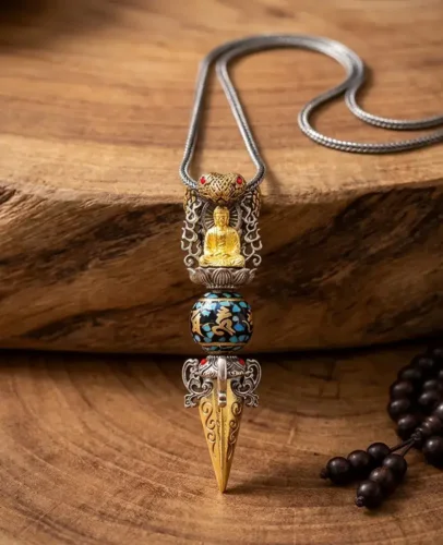 Tibetan Buddhist copper vajra dorje pendant necklace with gold Buddha figure, rotating Om Mani Padme Hum turquoise mantra bead, and engraved copper tip, displayed on natural wood surface with mala prayer beads