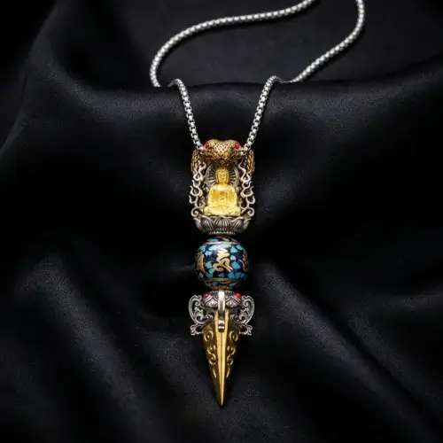 Close-up of Tibetan Buddhist vajra pendant necklace featuring a gold meditation Buddha, hand-painted blue Om Mani Padme Hum mantra bead with turquoise mosaic inlay, and copper dorje point on black silk background