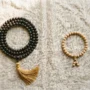 mala-necklace-vs-wrist-mala-comparison Flat lay product photography, top-down view. A full 108-bead mala necklace made of dark bodhi seeds with a golden tassel, arranged in a circular loop on the left side. On the right side, a 27-bead wrist mala bracelet made of light sandalwood beads with a small guru bead. Both items on a textured natural linen cloth with soft warm morning light from the upper left. Minimal, clean composition with generous negative space between items. Soft shadows. No text. Lifestyle spiritual aesthetic. Shot on medium format camera, f/4.0, warm neutral tones.