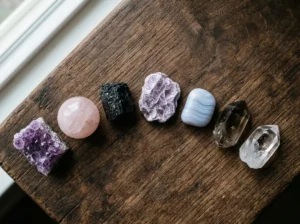 Seven healing crystals for anxiety arranged on a dark wooden surface — amethyst, rose quartz, black tourmaline, lepidolite, blue lace agate, smoky quartz, and clear quartz