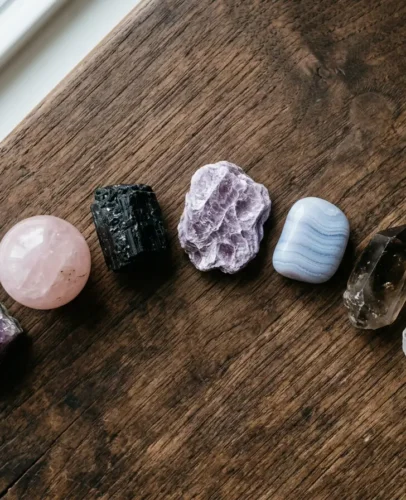 Seven healing crystals for anxiety arranged on a dark wooden surface — amethyst, rose quartz, black tourmaline, lepidolite, blue lace agate, smoky quartz, and clear quartz