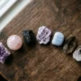 Seven healing crystals for anxiety arranged on a dark wooden surface — amethyst, rose quartz, black tourmaline, lepidolite, blue lace agate, smoky quartz, and clear quartz