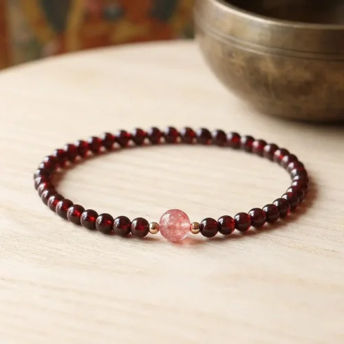 Natural red garnet beaded bracelet with pink strawberry quartz center bead and gold-filled spacers on wooden surface beside a Tibetan singing bowl