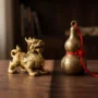 Pixiu vs Wu Lou_ Two Feng Shui Symbols Side by Side A side-by-side comparison of Pixiu and Wu Lou — a golden dragon-lion mythical creature (Pixiu) on the left and a brass calabash gourd (Wu Lou) on the right, displayed on a dark wooden surface with soft warm lighting