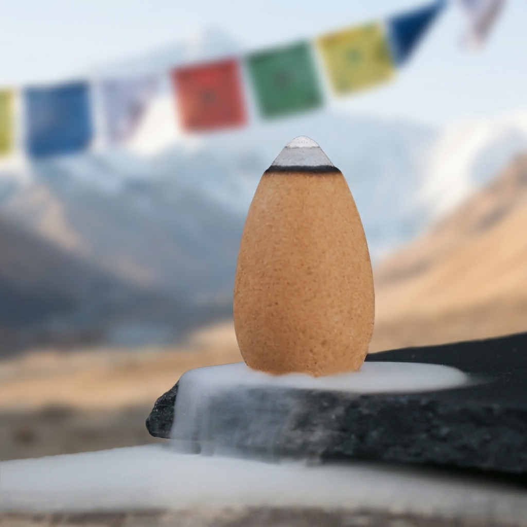 Teardrop Backflow Incense Cone with Tibetan Mountain Background Single beige teardrop-shaped backflow incense cone with white tip on stone base, Tibetan prayer flags and mountain landscape in soft focus background