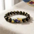 Tibetan Buddhist feng shui black obsidian Pixiu bracelet with gold-painted mantra beads and cloisonné Pixiu charm, resting on linen surface with Tibetan flag in background