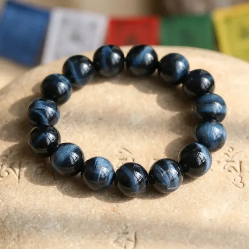 Blue Tiger Eye bracelet with natural chatoyancy displayed on carved Tibetan stone, colorful prayer flags in the background — PotalaStore