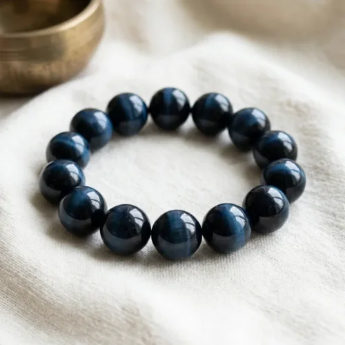 Natural Blue Tiger Eye beaded bracelet (10mm) resting on white linen cloth beside a brass Tibetan singing bowl — PotalaStore