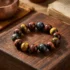 Multi-color tiger's eye protection bracelet with yellow, red and blue Hawk's Eye 10mm beads, displayed on a carved Tibetan wooden block beside a singing bowl and ancient scripture