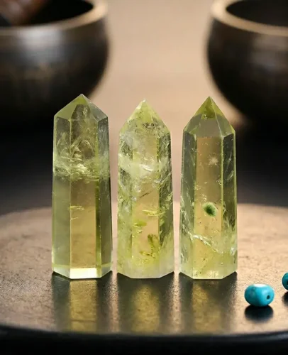 Three pale lemon-yellow natural citrine crystal towers displayed on dark surface flanked by Tibetan singing bowls and turquoise beads, showcasing natural feather inclusions and genuine unheated color
