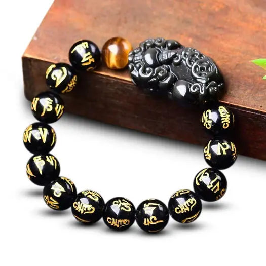 obsidian-pixiu-mantra-bracelet-on-wood-surface Obsidian Pixiu feng shui bracelet with gold Om Mani Padme Hum engraving resting on rustic wooden surface, lifestyle shot