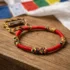 Handmade red Tibetan Buddhist monk bracelet with multicolor sacred knots displayed on rustic wood surface with colorful Tibetan prayer flags in background