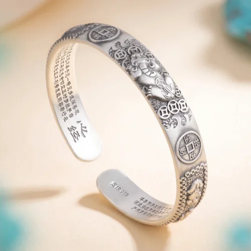Close-up of Fortune Pixiu Lucky Bangle showing the Heart Sutra engraved on the inner band and the č¶łé“¶999 fine silver hallmark stamp, with turquoise stones in background