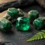 May Birthstone Natural Emerald Gemstones Raw and polished natural emerald gemstones with deep green color, displayed on dark stone surface with soft golden light — May 2026 birthstone guide by Potala Store