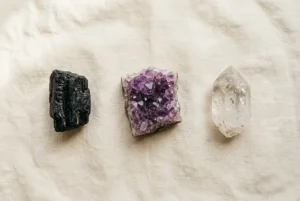 Three beginner crystals laid out on linen: clear quartz, purple amethyst, and black tourmaline