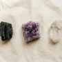 Three beginner crystals laid out on linen: clear quartz, purple amethyst, and black tourmaline