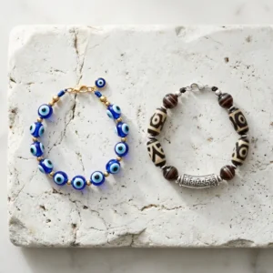 A Turkish nazar evil eye bracelet and a Tibetan dzi bead mantra bracelet placed side by side on a natural stone surface, representing two ancient spiritual protection traditions