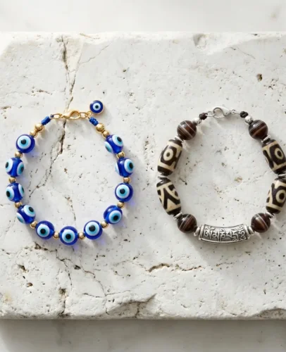 A Turkish nazar evil eye bracelet and a Tibetan dzi bead mantra bracelet placed side by side on a natural stone surface, representing two ancient spiritual protection traditions
