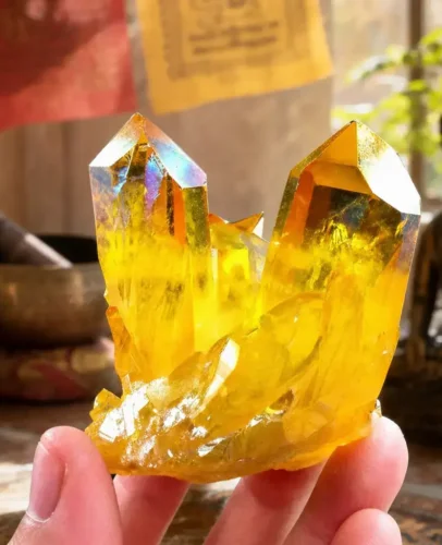 Hand holding a natural citrine wealth crystal cluster in front of Tibetan prayer flags, singing bowl, and Buddha statue — monastery-blessed by PotalaStore