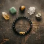 pixiu-bracelet-crystal-pairing-wealth Black obsidian Pixiu bracelet surrounded by citrine, green jade, tiger's eye, and clear quartz crystals arranged on a dark wood surface