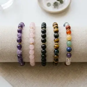 A row of beaded crystal bracelets in amethyst, rose quartz, black obsidian and tiger's eye on linen
