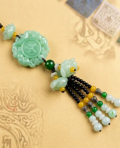 Green Jade Pixiu Car Charm Top View on Tibetan Scripture Top-down view of green jade Pixiu car charm showing carved coin medallion, twin jade lotus blossoms and tasseled jade beads