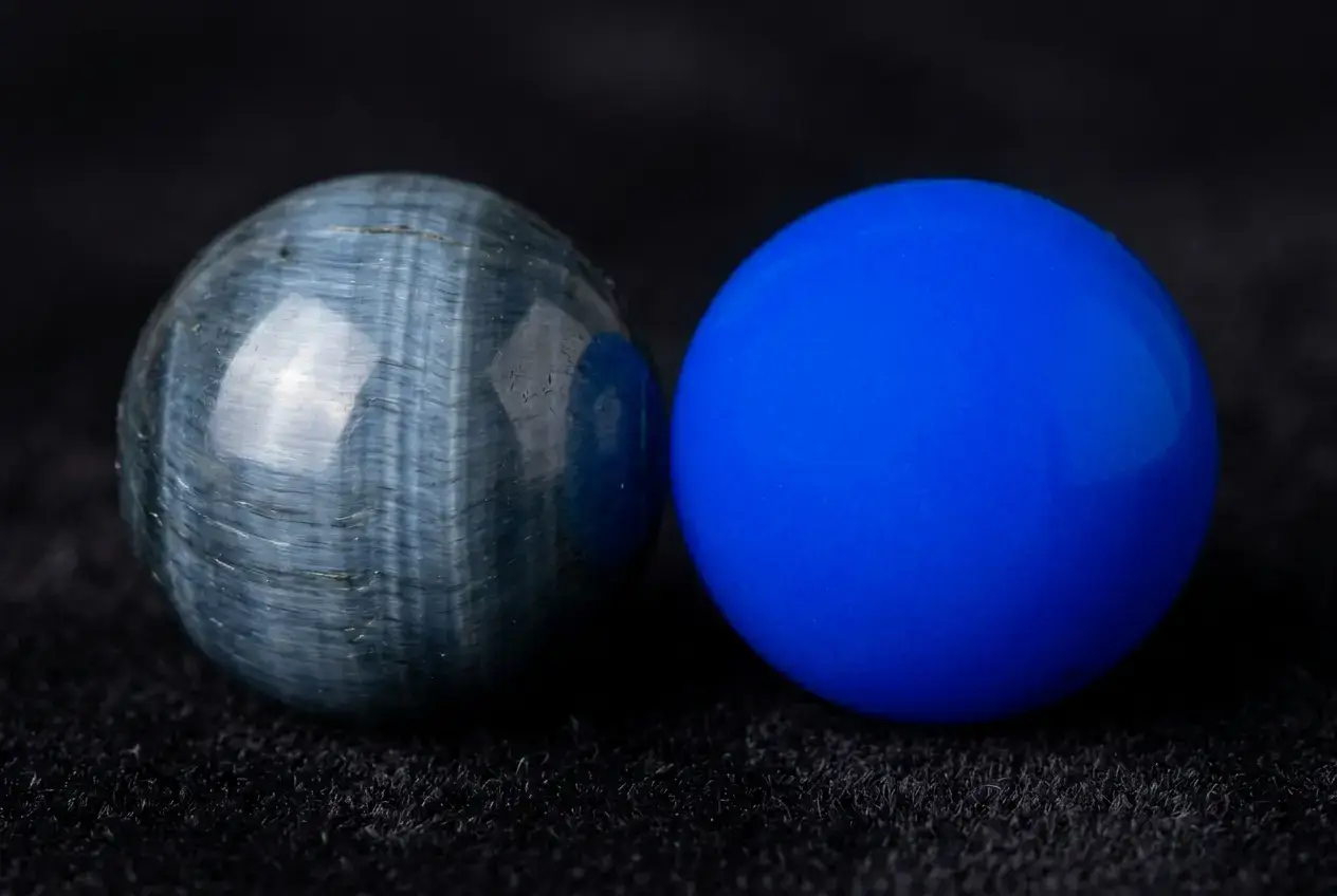 Close-up macro comparison of natural smoky blue tiger eye beads versus electric dyed blue beads