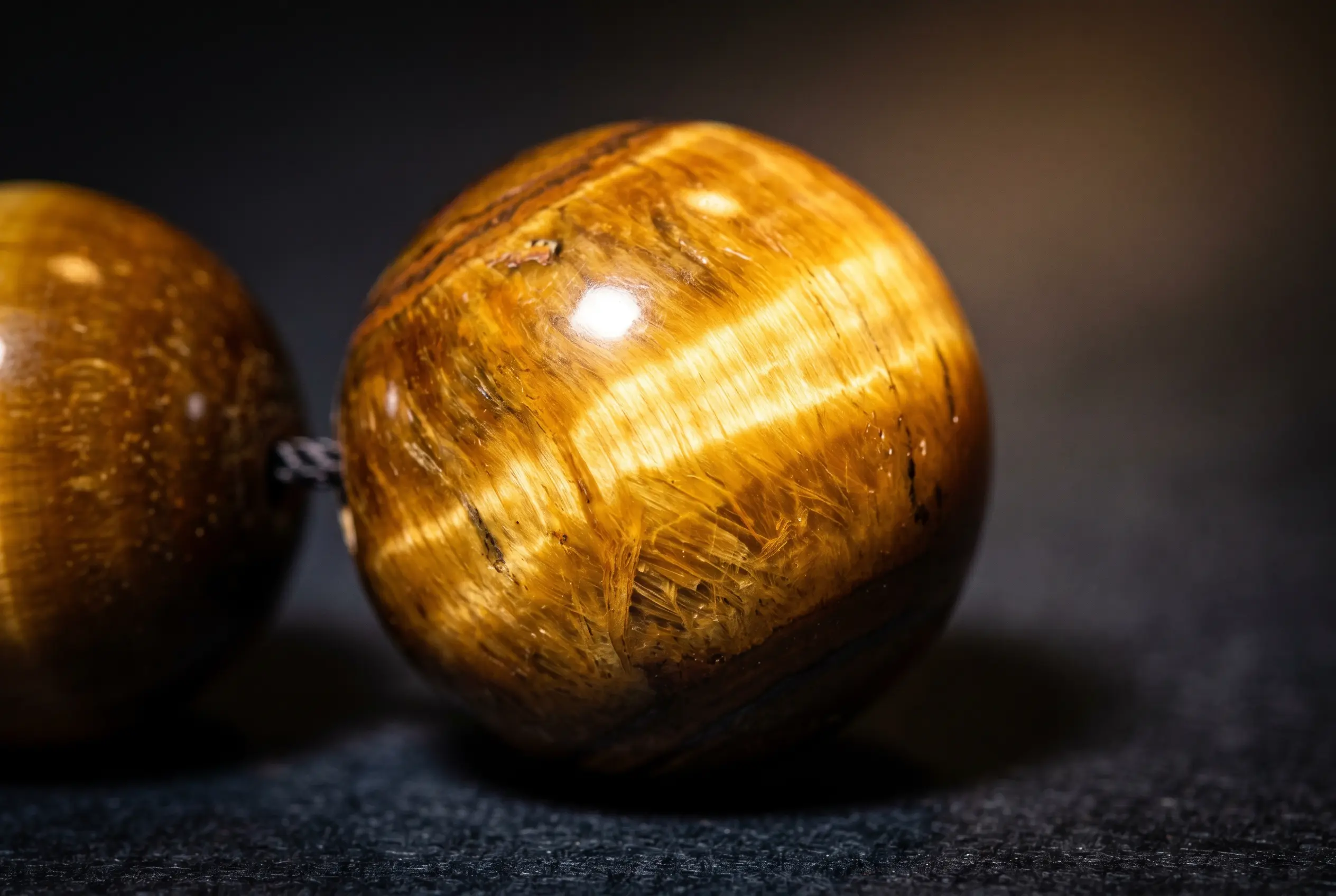 Tiger's eye bead tilted under light showing a moving silky golden cat's-eye band that proves it is genuine
