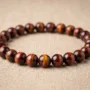 Red Tiger Eye Bracelet Showing Natural Chatoyancy Polished red tiger eye bracelet with reddish-brown bands and golden cat's eye shimmer on neutral background