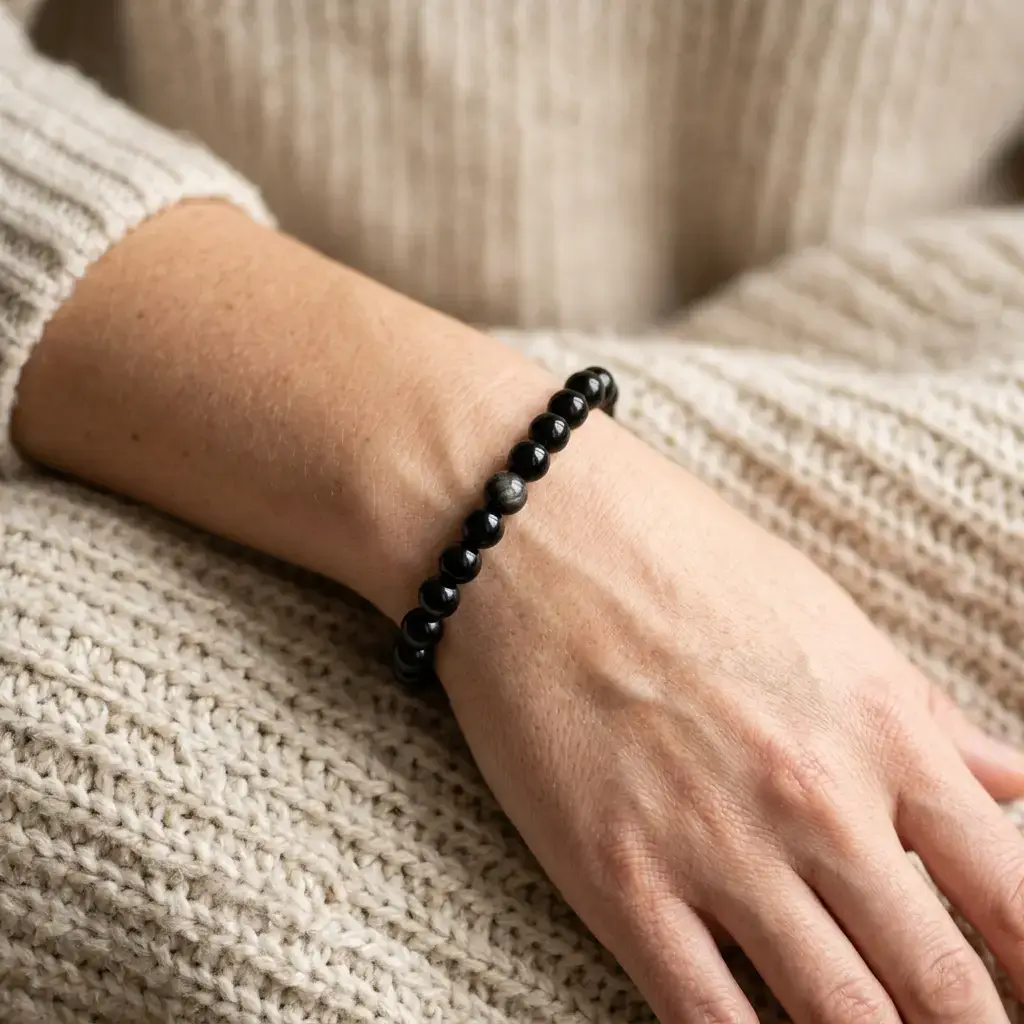 Beaded black obsidian bracelet worn on a person's left wrist against a neutral sweater