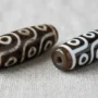 real-vs-fake-dzi-beads-comparison Real agate dzi bead next to a fake resin dzi bead, showing differences in etching depth and surface texture