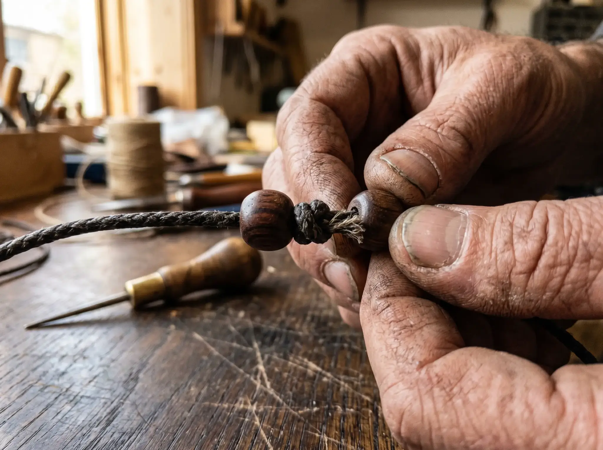 Close-up of hands tying a traditional Brahmagranti knot between beads while stringing a Tibetan mala