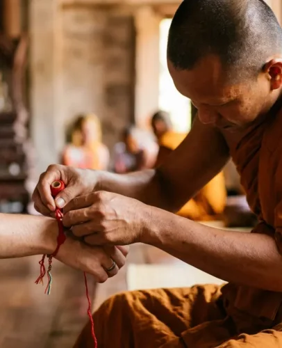 buddhist-monk-bracelet-meaning-hero Buddhist monk tying a red blessed bracelet onto a person's wrist as a blessing