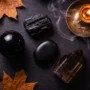 dark-crystals-protection-halloween-flatlay Four dark protective crystals — black obsidian, black tourmaline, black onyx, and smoky quartz — arranged in a flat lay on dark slate with dried autumn leaves and a lit candle