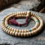 yak-bone-mala-beads-108-strand-tibetan Yak bone mala beads coiled in a spiral, showing 108 cream bone beads and a larger guru bead with tassel
