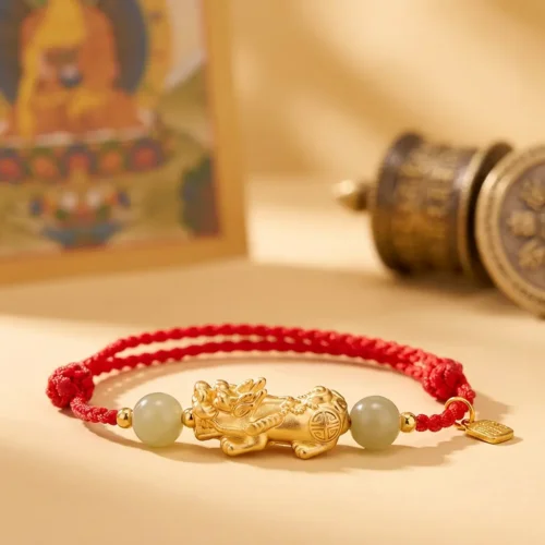 Copper Pixiu red string bracelet with jade beads and Fu tag beside a Tibetan thangka painting and prayer wheel