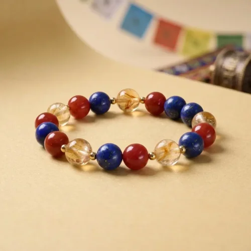 Bracelet extensible en pierres précieuses naturelles composé de perles de lapis-lazuli, d'agate rouge et de citrine, à côté d'une roue de prière tibétaine et de drapeaux de prière colorés.