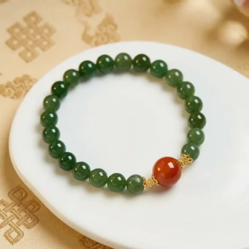 Hetian jasper and red agate luck bracelet with 8mm jade beads on a white dish, Tibetan endless knot cloth behind