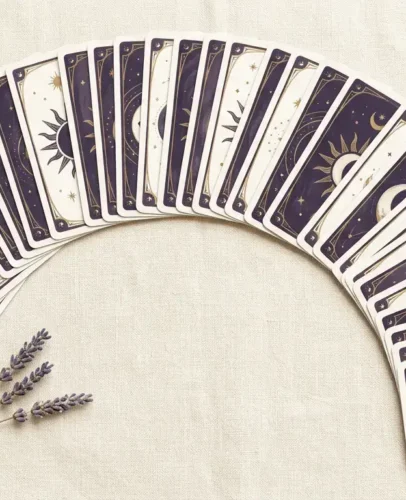 Full 78-card tarot deck fanned in an arc on cream linen, with an amethyst crystal beside the Major and Minor Arcana