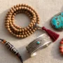 autentiske tibetanske smykker flatlay Fladt lay-out af autentiske tibetanske smykker: en håndhamret sølvmanchet, mala med 108 perler, turkis vedhæng, rød koral og en agat dzi-perle på linned