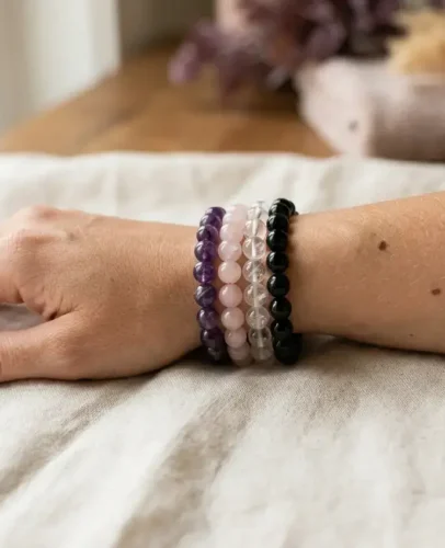A stack of four natural crystal bracelets, including amethyst and rose quartz, worn on a woman's wrist.