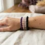 krystalarmbånd-stablet-på-håndleddet En stak af fire armbånd med naturlige krystal, inklusive ametyst og rosenkvarts, båret på en kvindes håndled.