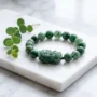 bracelet en jade vert Pixiu avec porte-bonheur lapin Cinq porte-bonheur pour le signe astrologique du Lapin en 2027, année de la Chèvre de Feu, comprenant un bracelet de jade, un cordon rouge et un pendentif Manjushri disposés sur une surface en bois sombre.