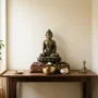 domácí-buddhistický-oltář-v-úrovni-očí Malý domácí buddhistický oltář s bronzovou sochou Buddhy umístěnou nad úrovní očí sedícího člověka, tenkou stopou kadidlového kouře a jedinou obětní miskou na dřevěném konzolovém stolku