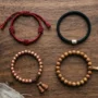 tibetan-bracelet-types-comparison.webp Four Tibetan bracelet styles laid flat: red knotted cord, mantra bracelet, copper bead bracelet and 21-bead wrist mala